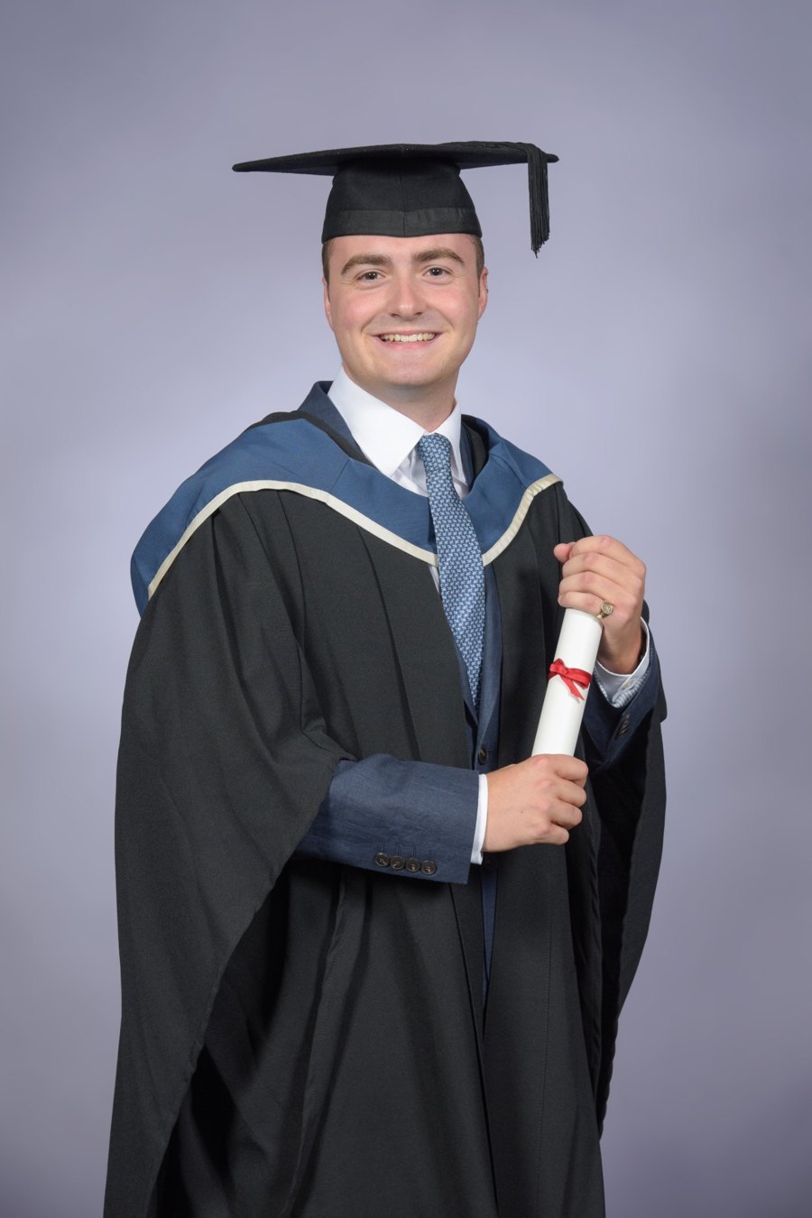 Hugo King in graduation cap and gown, holding his degree scroll